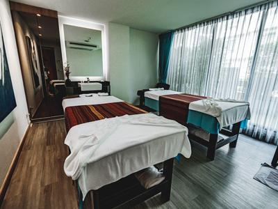 Modern spa room with two massage tables, wood flooring, and large windows with curtains.