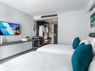 Modern hotel room with double bed, blue pillows, and wall-mounted flat screen TV.