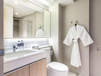 Modern hotel bathroom with large mirrors and white bathrobe hanging on the wall.