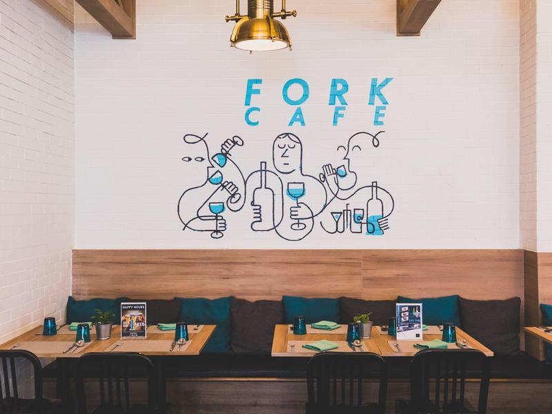 Cozy café with wooden bench, tables, and colorful wall art 'Fork Café' on white wall.