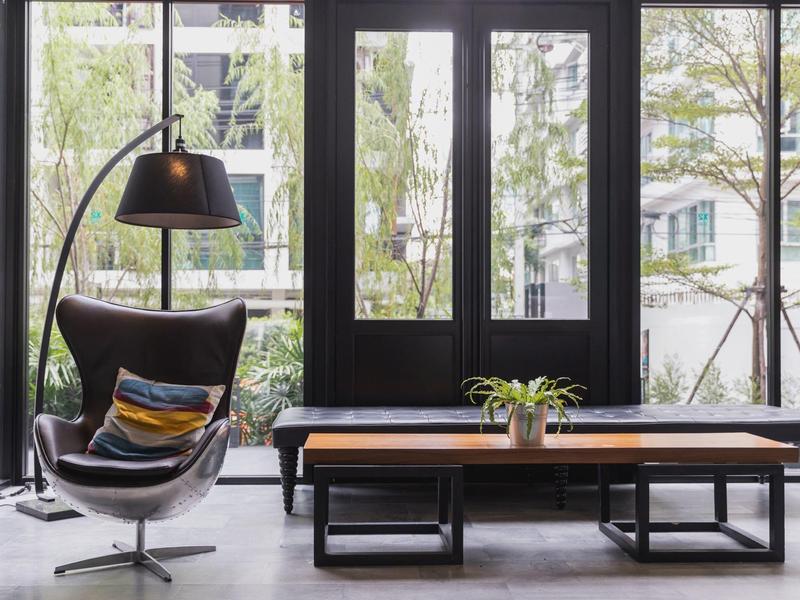 Modern lounge area with black chair, low wooden table, and large windows overlooking the outside.