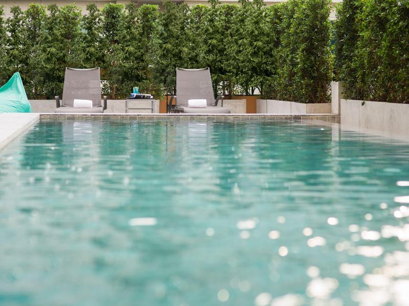 Clear swimming pool with lounge chairs and green privacy screen in background.