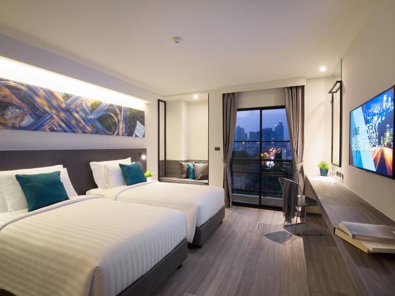 Modern hotel room with two beds, desk, and balcony with city view.