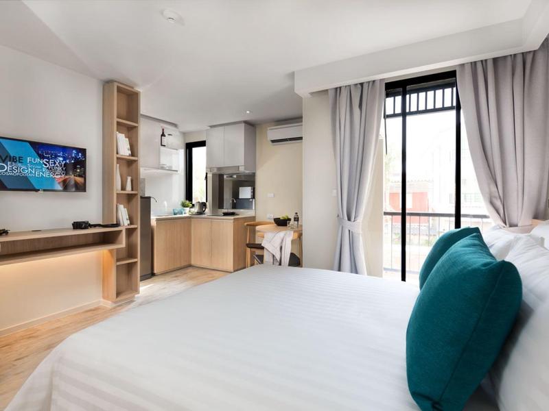 Modern hotel room with large bed, blue pillows, and balcony overlooking outside.