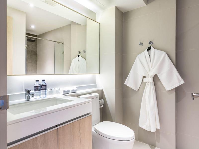 Modern hotel bathroom with large mirrors and white bathrobe hanging on the wall.