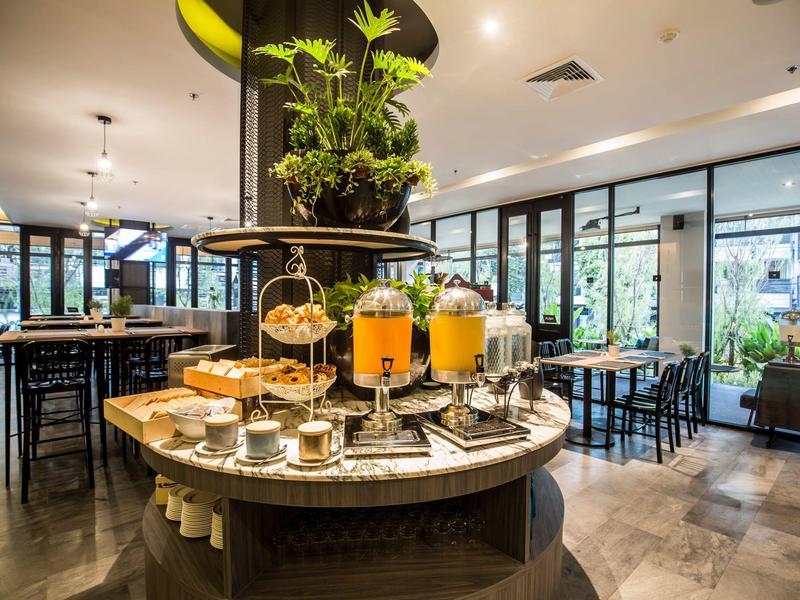 Buffet with juices and pastries in a modern hotel restaurant with large windows.