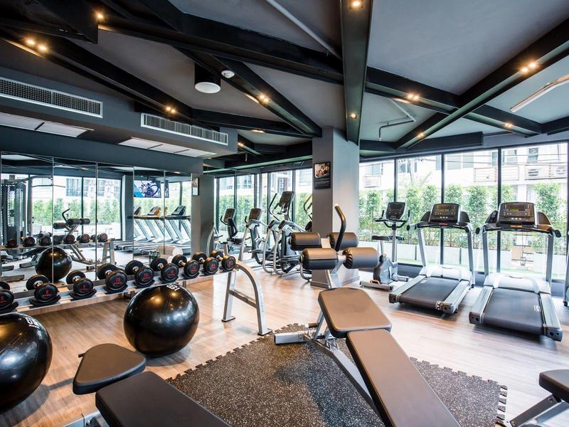 Modern gym with workout equipment, cardio machines, and large windows overlooking outdoors.