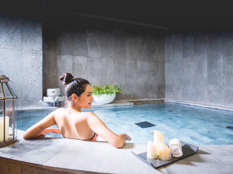 Woman relaxing in a modern spa pool with candles and calm atmosphere.