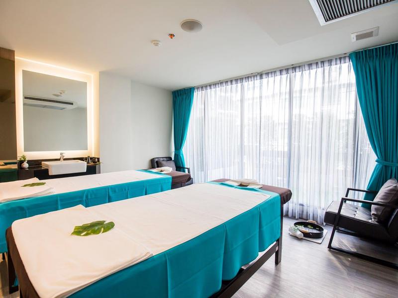 Modern treatment room with two massage tables, large windows, and turquoise curtains.