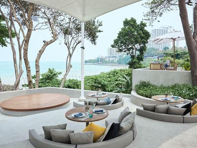 Outdoor lounge area with round seating and sea view, surrounded by trees.