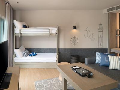 Modern hotel room with bunk bed, sofa area, and maritime decor in neutral tones.