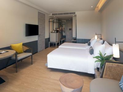Bright hotel room with two double beds, seating area, and modern design.