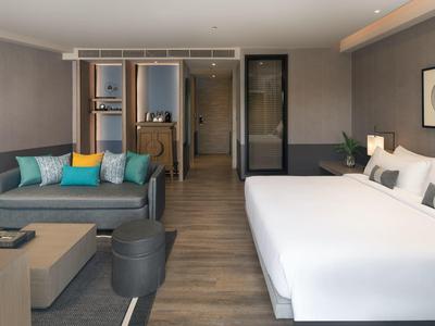 Modern hotel room with large bed, seating area, and open bathroom area.