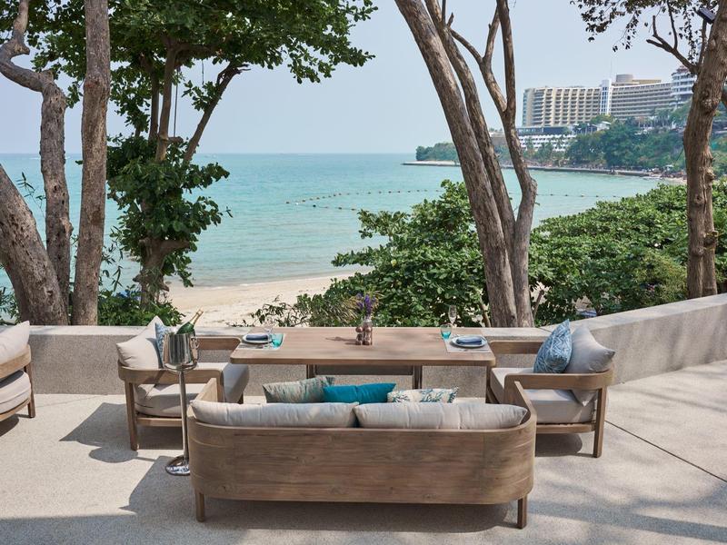 Terrace with seating furniture and sea view, surrounded by trees and sandy beach.