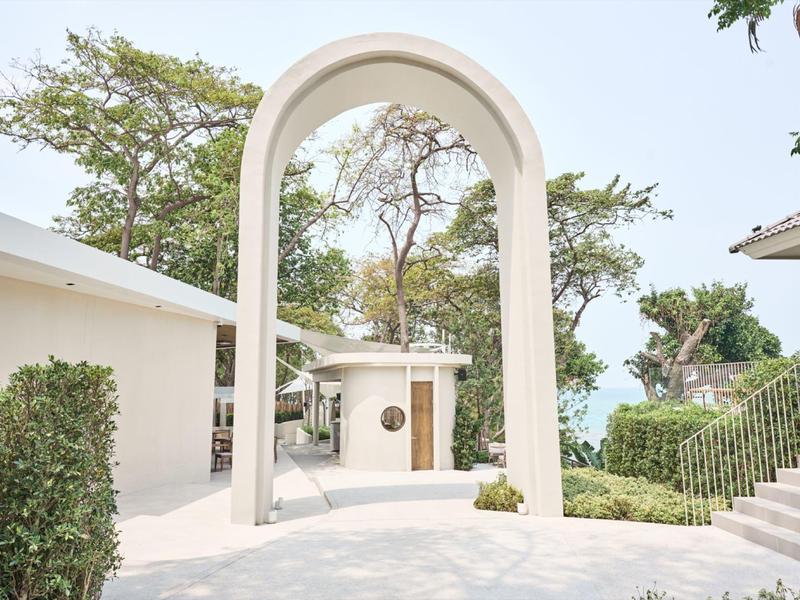 Bright outdoor area with white arch, surrounded by buildings and trees.