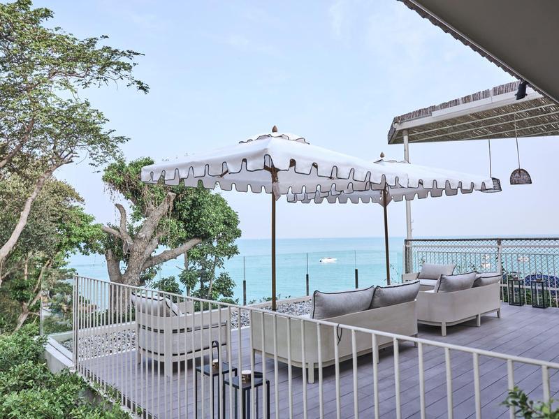 Terrace with umbrellas and seating overlooking the sea and trees.