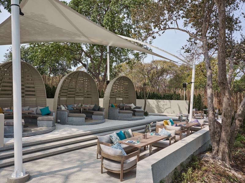 Modern outdoor area with round lounge pods and seating under shade sails.