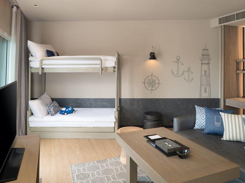 Modern hotel room with bunk bed, sofa area, and maritime decor in neutral tones.
