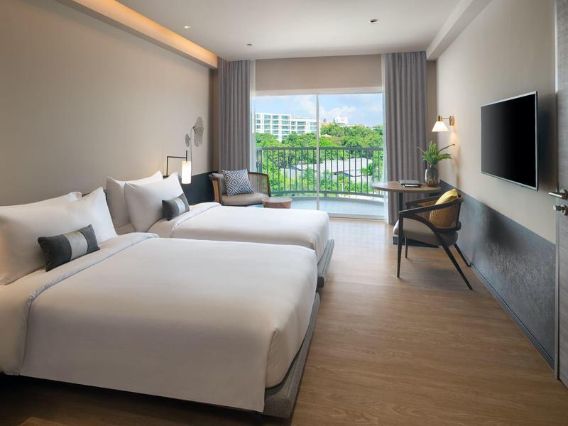 Modern hotel room with two double beds, seating area, and large window overlooking greenery.