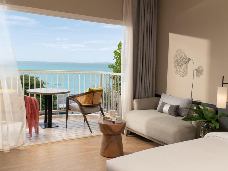 Modern hotel room with sea view and balcony seating area.
