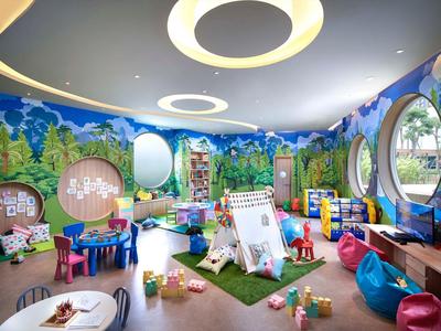 Sala giochi colorata per bambini con giocattoli, tavoli e finestre rotonde sulle pareti.