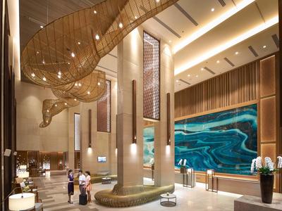 Luxusní hotelová hala s vysokým stropem, moderním osvětlením a velkým uměleckým dílem na stěně.