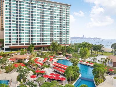 Grande hotel con più piscine, ombrelloni rossi e vista sul mare in una giornata di sole.