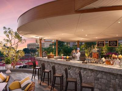 Area bar esterna moderna con posti a sedere e vista sulla città al tramonto.