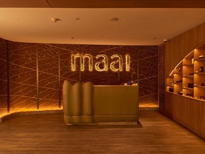 Area accoglienza elegante con banco dorato e insegna illuminata 'maal'.