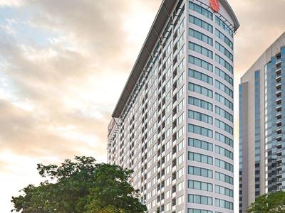 Alto edificio di hotel con tetto distintivo e alberi in primo piano al tramonto