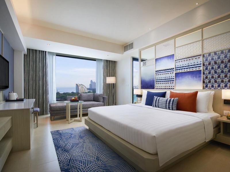 Camera d'hotel moderna con letto grande, tappeto blu e finestra panoramica con vista città.