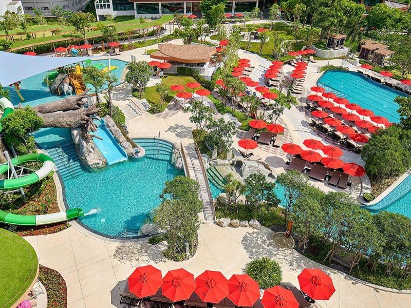 Complesso acquatico colorato con scivoli, piscina, lettini e verde circostante sotto il sole.