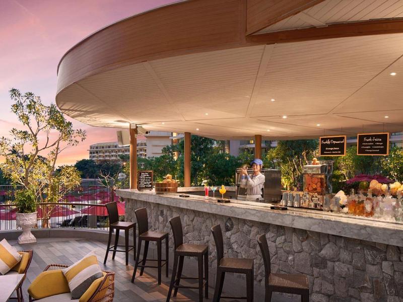 Area bar esterna moderna con posti a sedere e vista sulla città al tramonto.