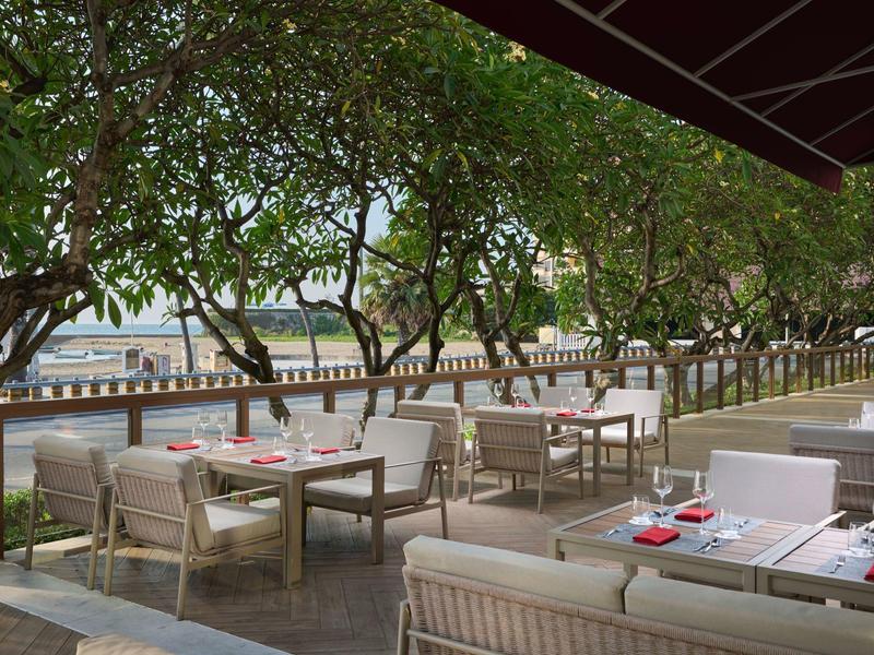 Ristorante all'aperto con aree salotto moderne e alberi accanto a un fiume.