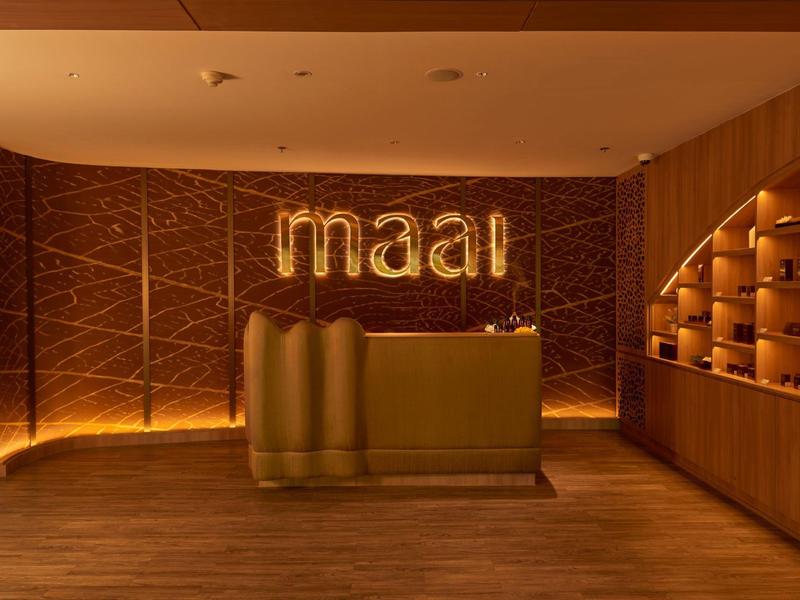 Area accoglienza elegante con banco dorato e insegna illuminata 'maal'.