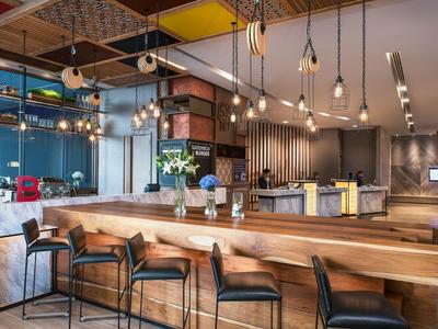 Elegante barra de hotel con mostrador de madera, taburetes modernos y lámparas colgantes en ambiente acogedor.