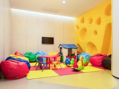 Área de juegos infantil colorida con pufs, juguetes y una casita pequeña en una habitación luminosa.