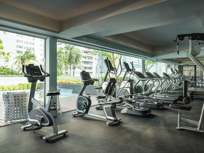 Gimnasio moderno con bicicletas estáticas y máquinas de ejercicio frente a grandes ventanales con vista al exterior.