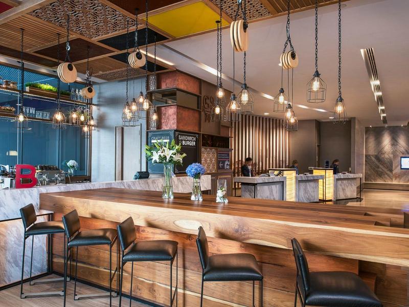 Elegante barra de hotel con mostrador de madera, taburetes modernos y lámparas colgantes en ambiente acogedor.