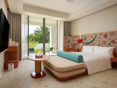 Helles Hotelzimmer mit großem Bett, Balkon und Blick auf grüne Bäume.
