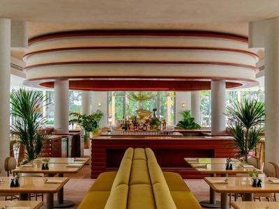 Modernes Hotelrestaurant mit runden Deckenakzenten, Pflanzen und gemütlicher Sitzbank in der Mitte.