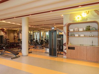Moderner Fitnessraum mit verschiedenen Geräten, Hanteln und hellen, warmen Farben.