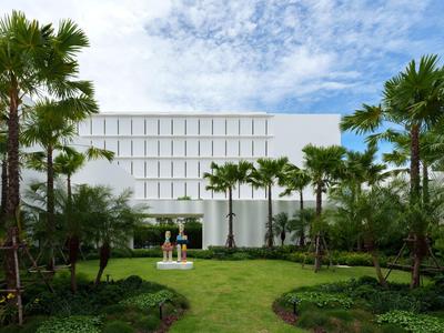Moderner Hotelkomplex mit weißem Gebäude, umgeben von gepflegtem Garten und Palmen unter blauem Himmel.