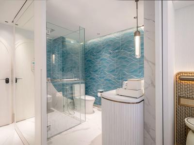 Modernes Badezimmer mit blauer Mosaikwand, Glasdusche und weißem Waschbecken im Hotel.