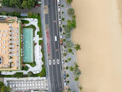 Luftaufnahme eines Hotels neben einer belebten Straße und einem breiten Sandstrand am Meer.
