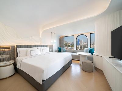 Modernes Hotelzimmer mit großem Bett, Fensterbankplatz und Blick auf Stadt und Meer.