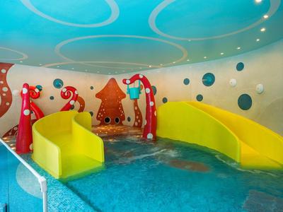 Buntes Innen-Pool mit gelben Rutschen und Wanddesign mit Pfeilen und Punkten.