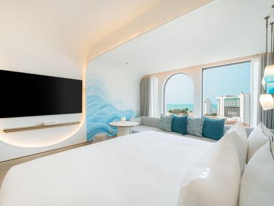 Modernes Hotelzimmer mit großem Bett, Wandkunst und Fenstern mit Blick auf die Stadt.