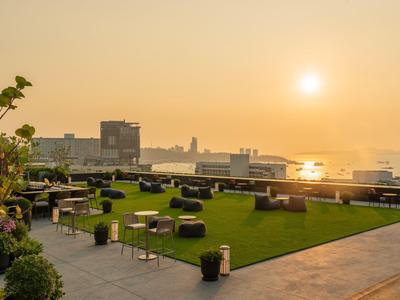 Dachterrasse mit Sitzbereichen und Blick auf Stadt und Sonnenuntergang am Meer.