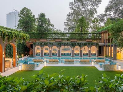 Moderner Hotelinnenhof mit Pool, grüner Wiese und Bäumen, umgeben von Arkadenbögen.